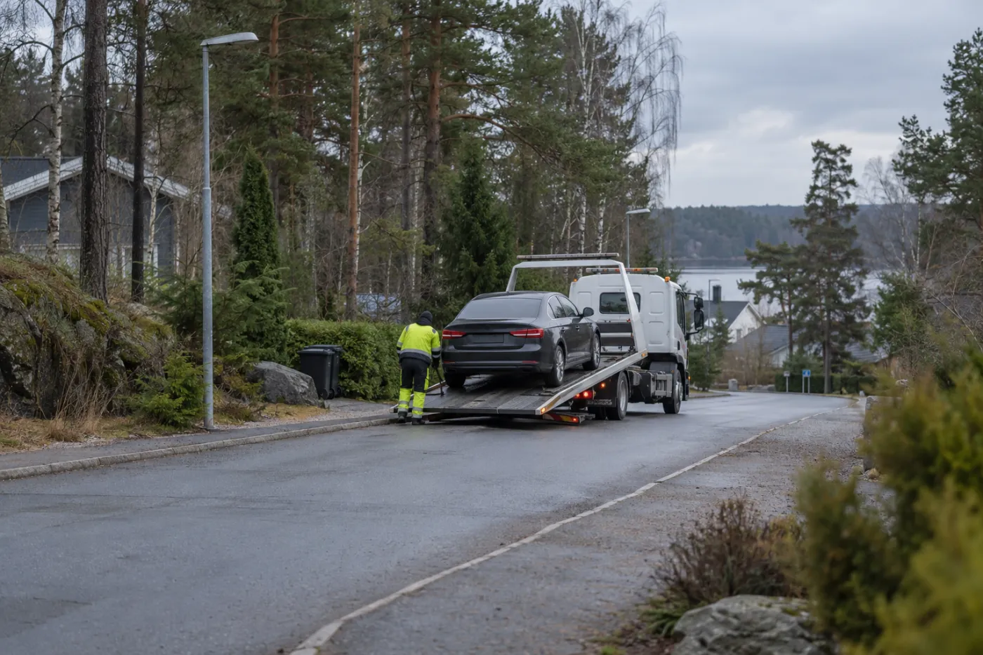 Bärgningsbil lastar en personbil på en väg kantad av skog