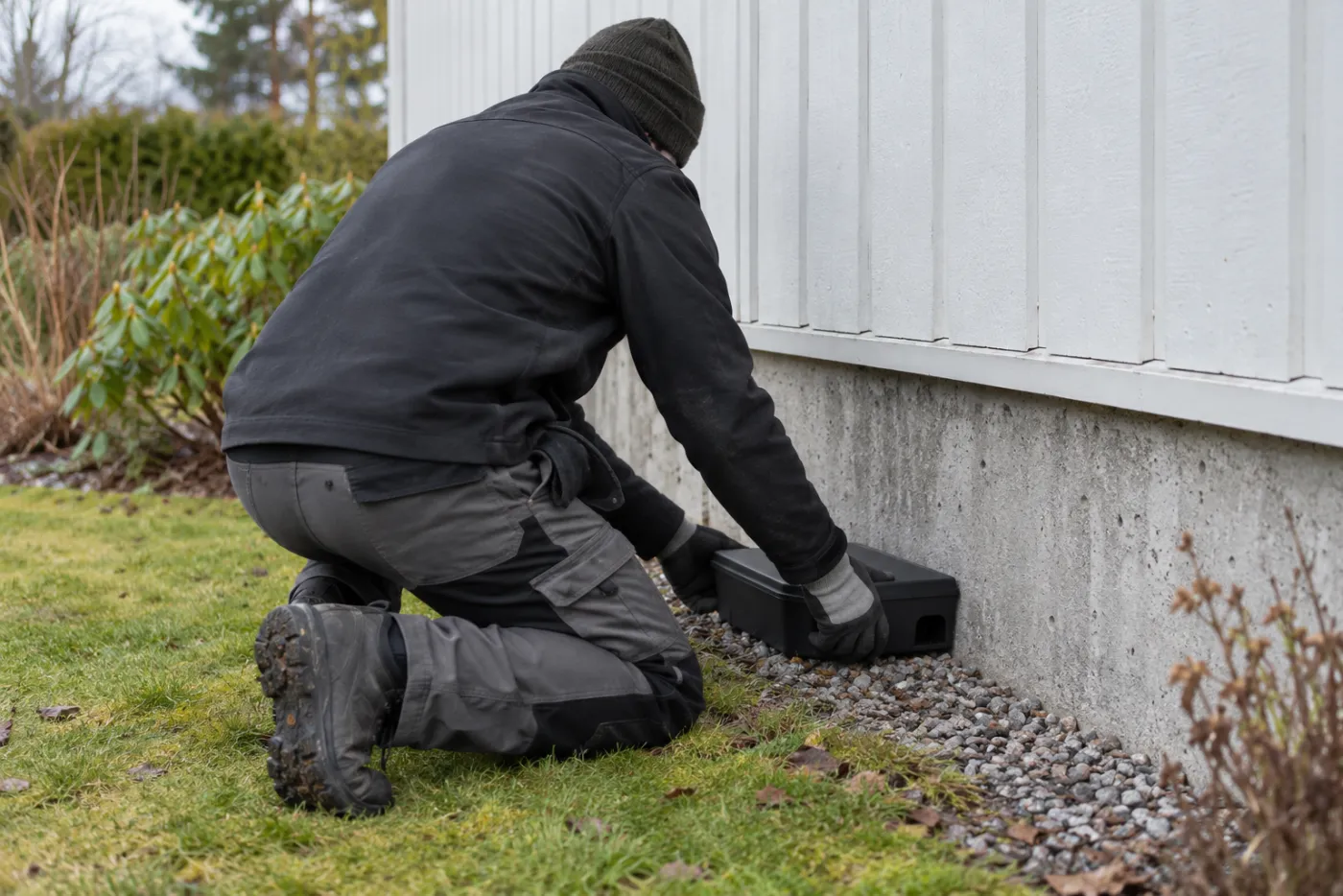 Skadedjurstekniker placerar en sluten betesstation längs husgrunden